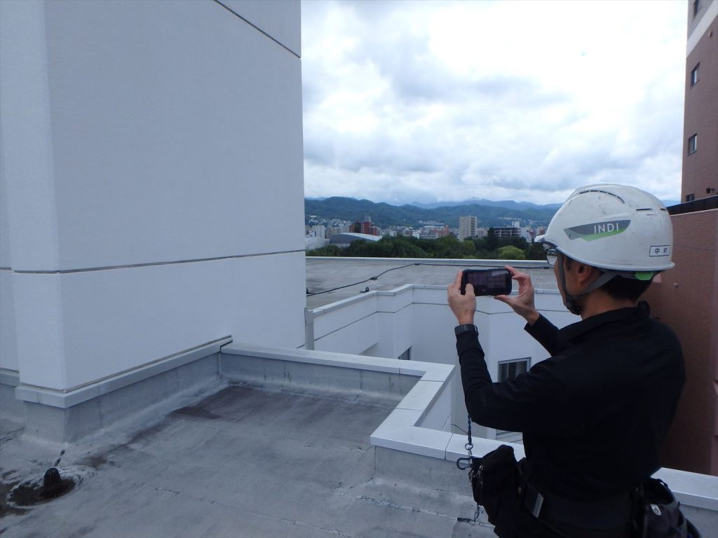 マンションの屋上で写真報告アプリを活用して調査を実施している様子